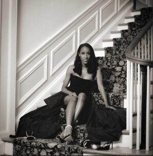 A person in a formal gown sits on a staircase, exuding elegance and sophistication. The scene is styled in a classic black-and-white motif.