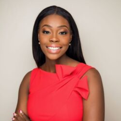 A person smiling in a professional headshot, wearing a red dress with a decorative bow on the shoulder, against a neutral background.