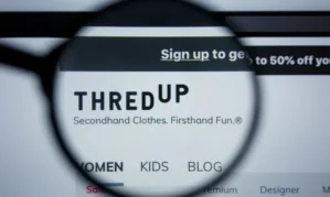 Magnifying glass focusing on the ThredUp website, highlighting the slogan "Secondhand Clothes. Firsthand Fun." and navigation options like Women, Kids, Blog.